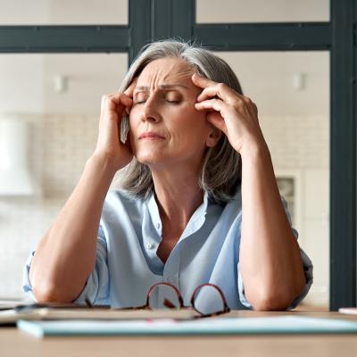 Senior person holds head in hands while at desk.