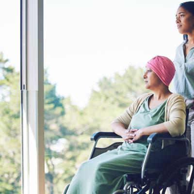 A woman in her 30s pushes another older woman in a wheelchair down a hallway.
