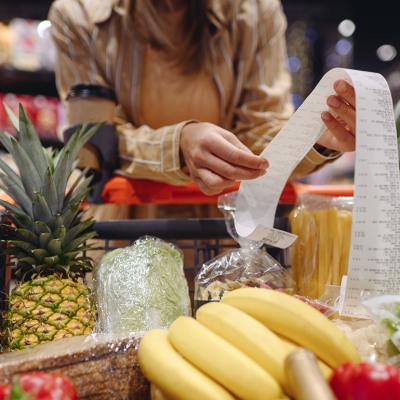 Woman leaning on a grocery cart while reading the receipt of her purchases.