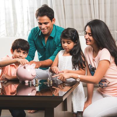 A family of four where parents are teaching their two kids how to save money in a piggybank.