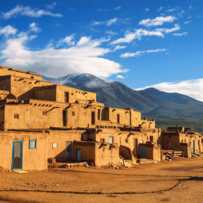 Ancient dwellings of UNESCO World Heritage Site Taos Pueblo in New Mexico with mountains in the background.