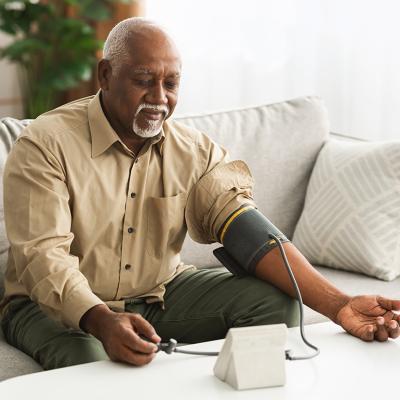 A senior black man measuring his blood pressure using a digital monitor.
