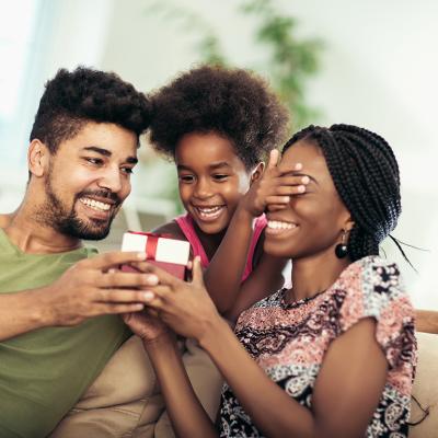 A happy black family surprising the mother with a box of jewelry as a mother's day gift.