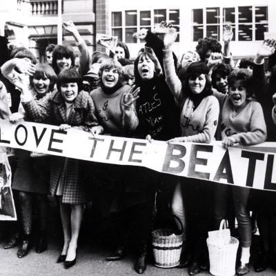 Screaming Beatles fans holding banners and waving at the band, circa 1964