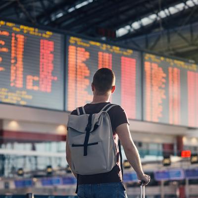 A man with a backpack looking at a departure and arrival schedule board in an airport.