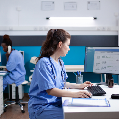 Nurse practitioners in scrubs filling out patient details on computers in a medical clinic