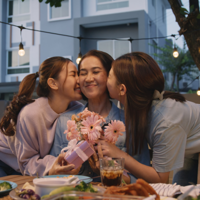 Two children embrace their mother and give her flowers at an outdoor dinner party