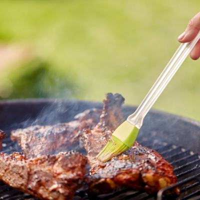 Close up shot of a hand basting barbecue meat on an outdoor grill