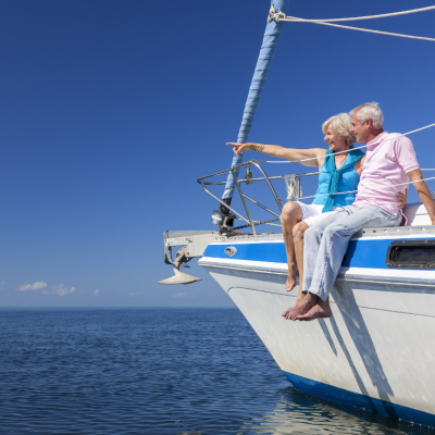 A happy senior couple sitting on the side of a sail boat on a calm blue sea looking and pointing to a clear horizon