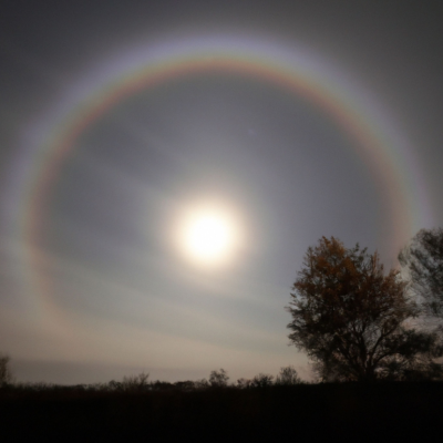 A lunar rainbow and a shining full moon against a clear, dark sky