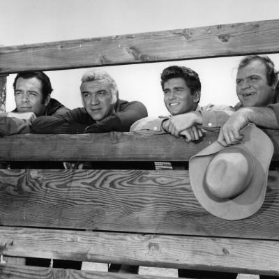 Dan Blocker holds his hat while standing with others in a scene from the TV series “Bonanza” (1959–1973).