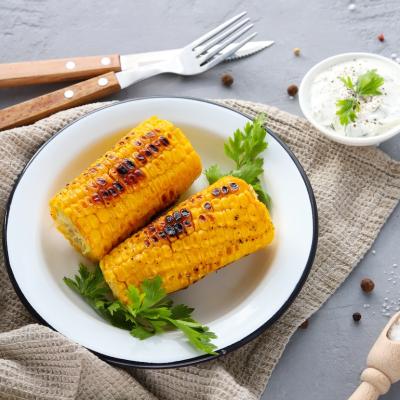 Grilled corn cobs with spices and sauce on a concrete background, top view.