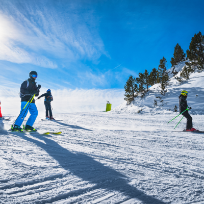 People skiing and snowboarding down a ski slope against a clear blue sky