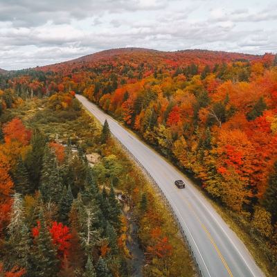 Drone shot of a car driving through fall foliage in New England