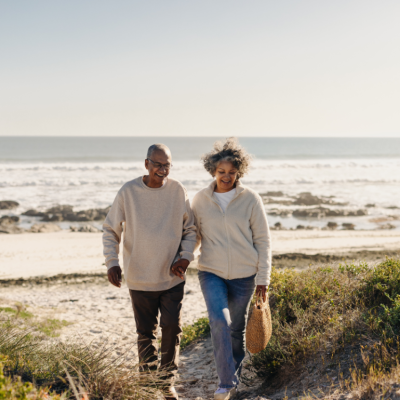 Cheerful elderly couple smiling happily while walking away from the beach after a picnic.
