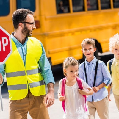 Traffic guard helping young school children cross the road in front of a school bus