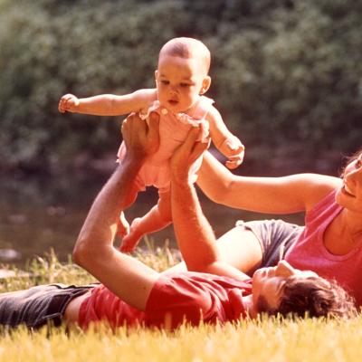 1970s couple laying in the grass holding baby up