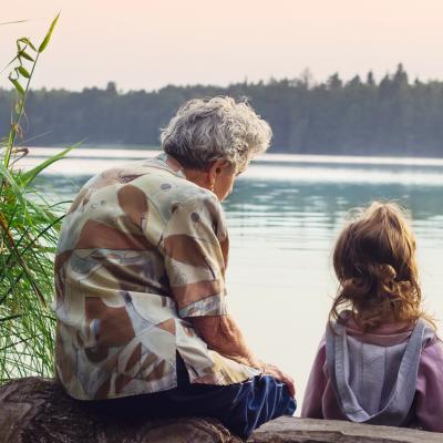 Grandparent sits with grandchild, overlooking the river on a warm day.