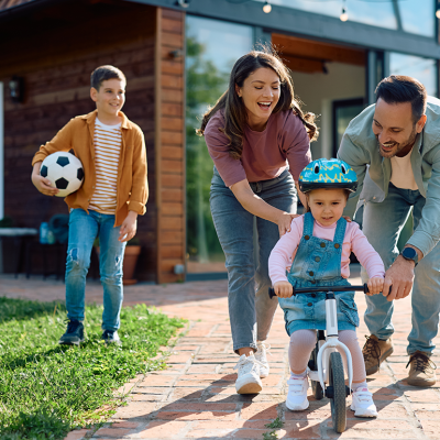 Child learning to ride bicycle with help of her parents.