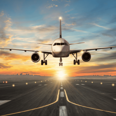 An airplane during its final approach for landing on a runway. Bright orange sun positioned low on the horizon. 