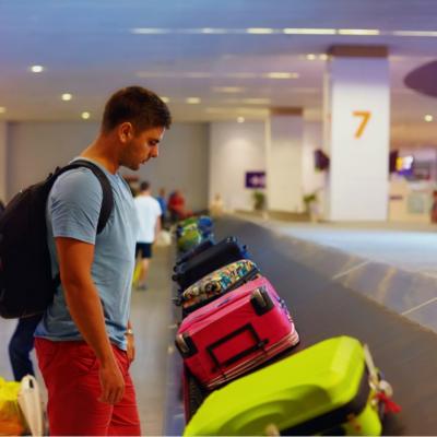 A young adult wearing a backpack looking down at the luggage carrousel with colorful bags.