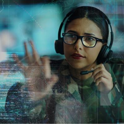 A woman wearing military camouflage and glasses, along with a headset. She is looking on the digital display in front of her.