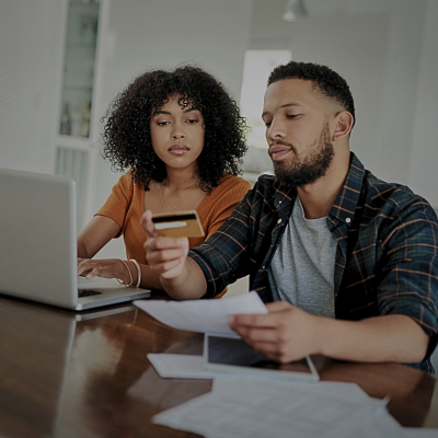 A young couple sitting at the table with a laptop, papers, and a credit card in front of them. 