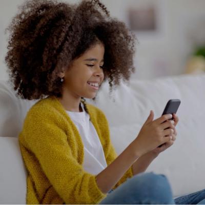 Preteen sitting on the couch at home looking at her cellphone and smiling.