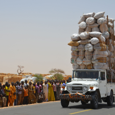 A truck loaded to the sky with donated food next to a street lined with people.