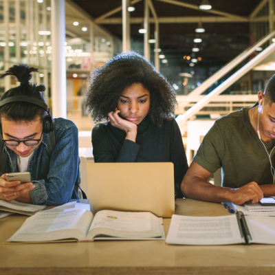 Three college students fixated on their laptops and smartphones.