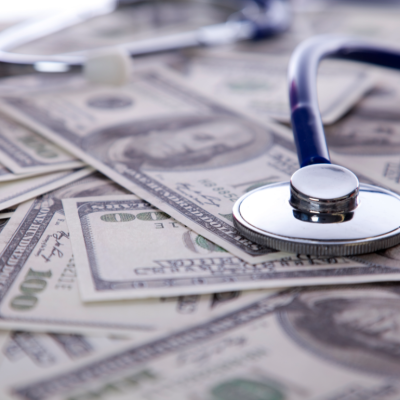 A stethoscope rests on a pile of one hundred dollar bills.