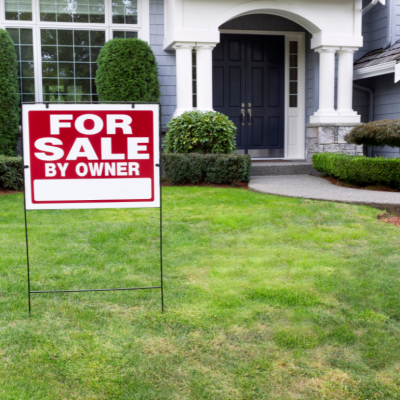 A for sale by owner sign in the front lawn of a suburban home. 