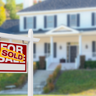 A for sale sign with a sold sticker in front of a white suburban house.