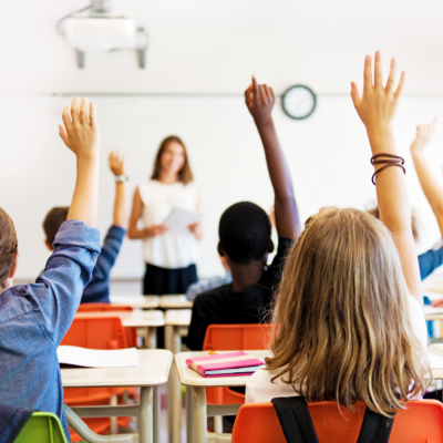 Kids in a classroom raising their hands.
