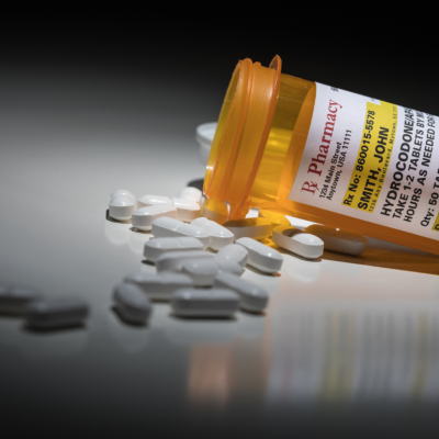 A prescription bottle for Hydrocodone on its side with pills spilling out.