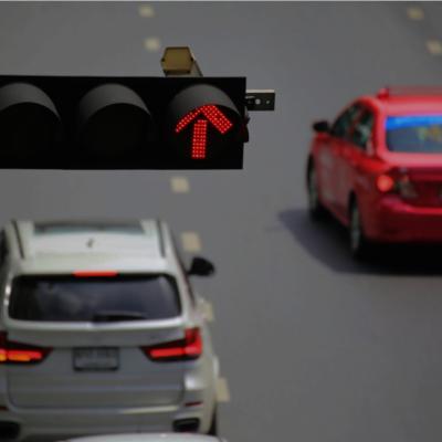 Traffic lights with a red light camera hanging above the road with two vehicles driving.