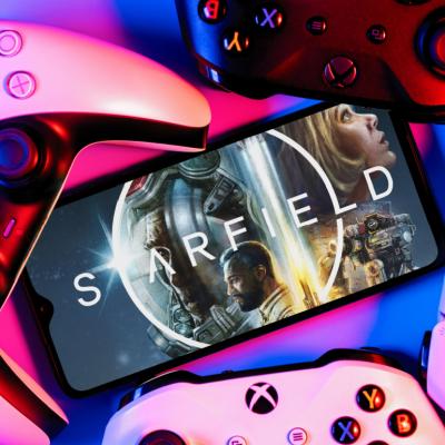 A smartphone with Starfield game logo on screen surrounded by gamepads.