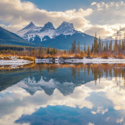 Three snowy mountain peaks reflected in the body of water in the foreground.