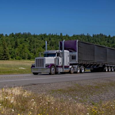 A large semi-truck driving along a highway in a rural area.