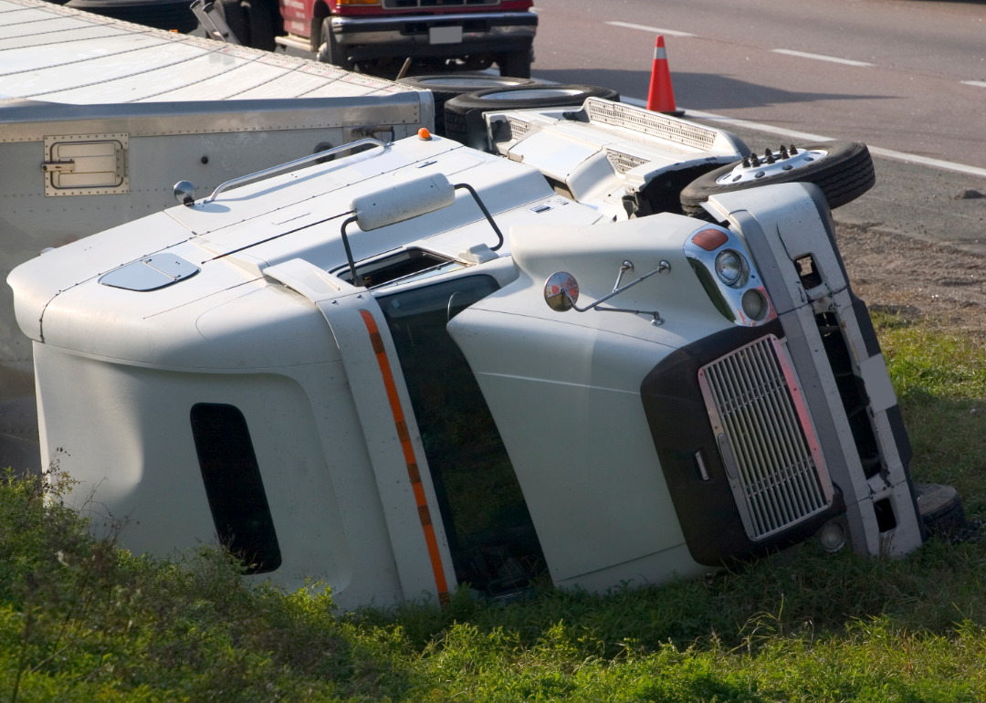 A white semi truck lies on its side on the edge of a highway