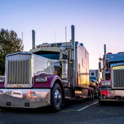Big rig trucks stand side by side in a parking lot at sunset.