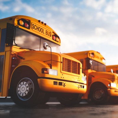 A row of school busses lined up under a blazing sun.