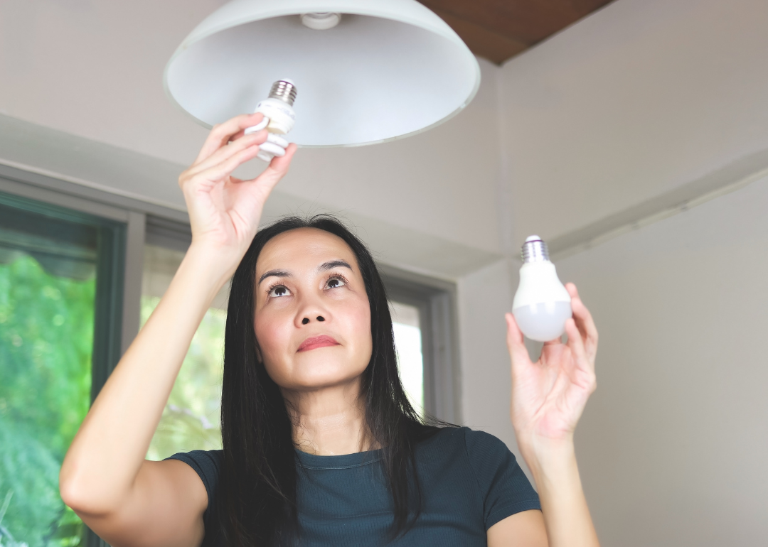 A person changing a light bulb from incandescent to spiral.