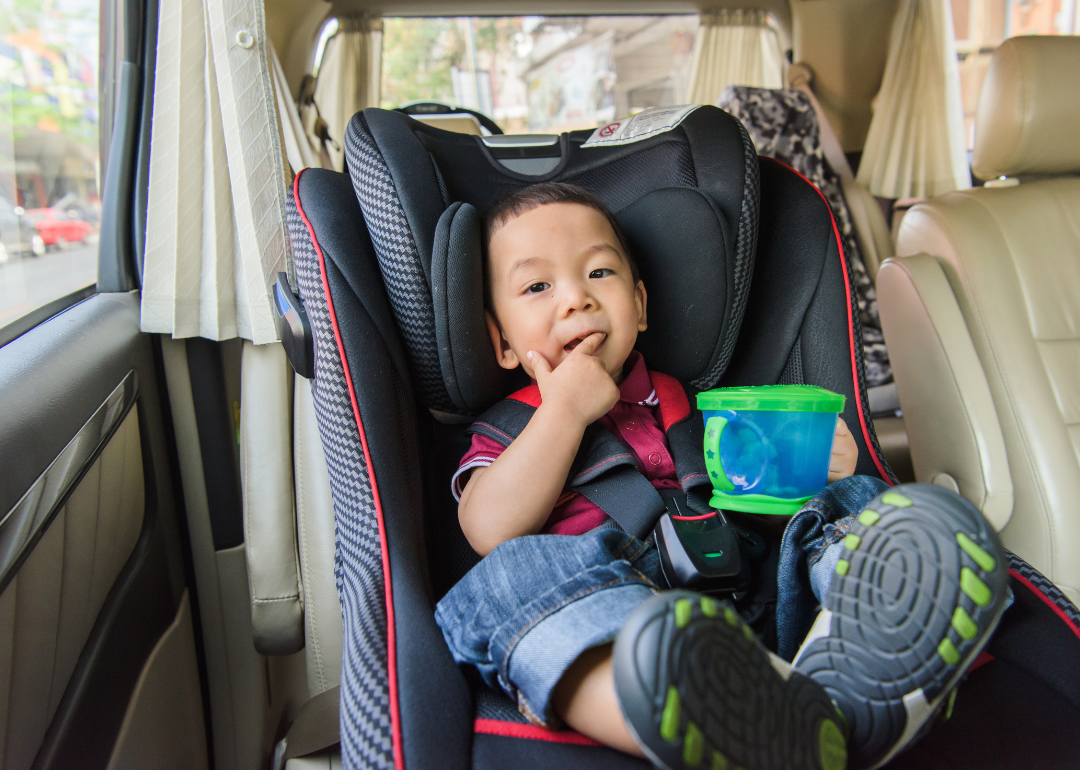 A baby in a car seat while eating a snack.