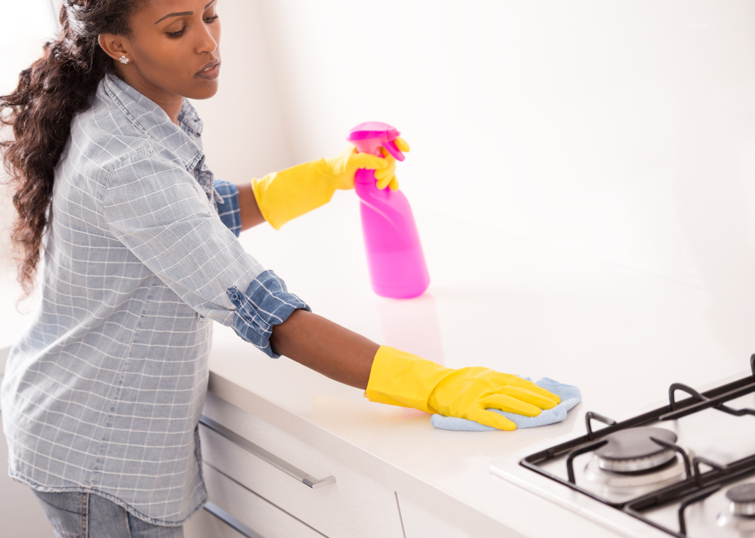 A woman wearing rubber gloves and folding a spray bottle of household cleaner