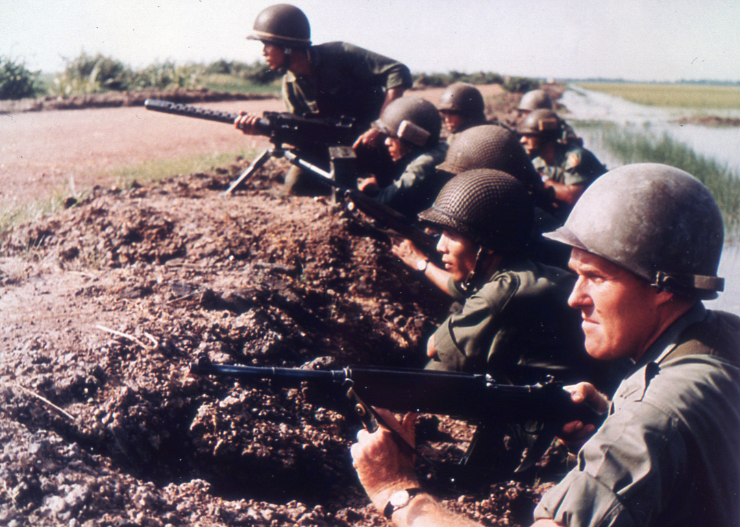 A US Army advisor and a line of Vietnamese infantrymen look into the distance along the bank of a rice paddy in 1965.