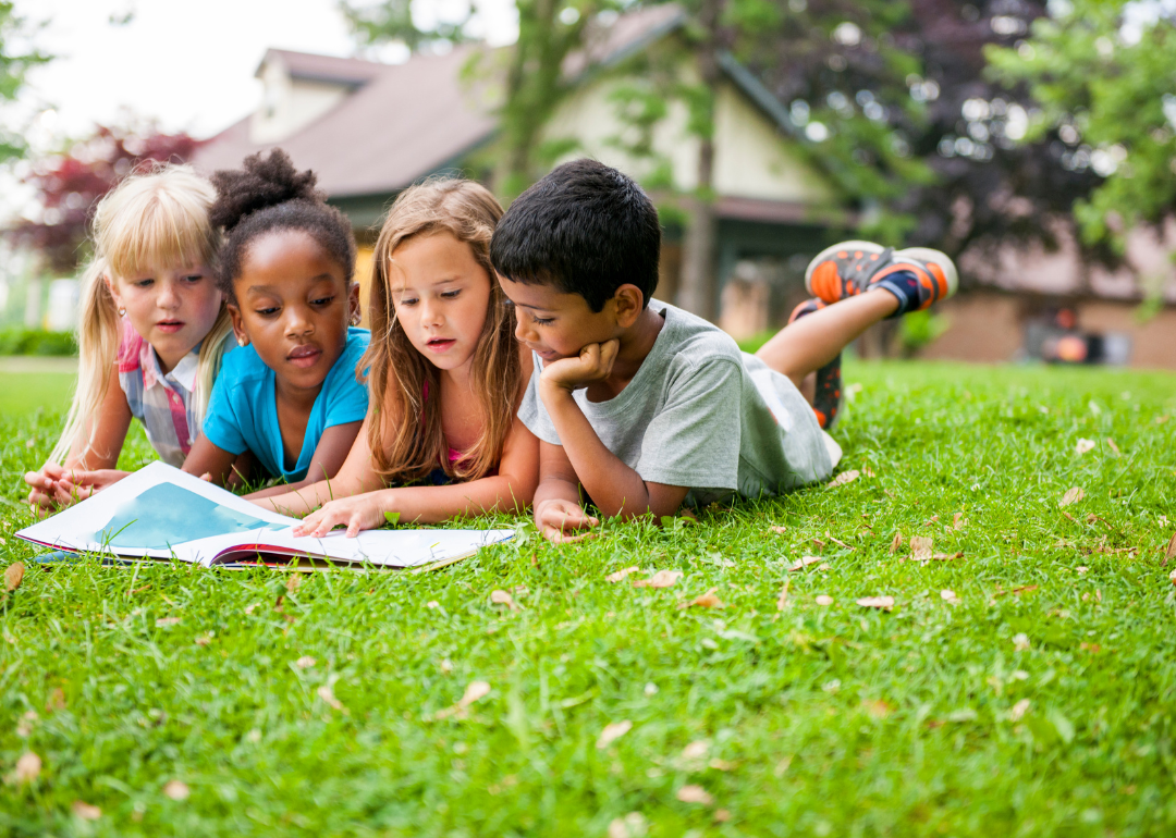 Four children reading a book together outside on a sunny day.