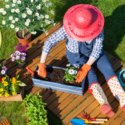 A person in a bright orange sun hat and polka dot rain boots gardening.