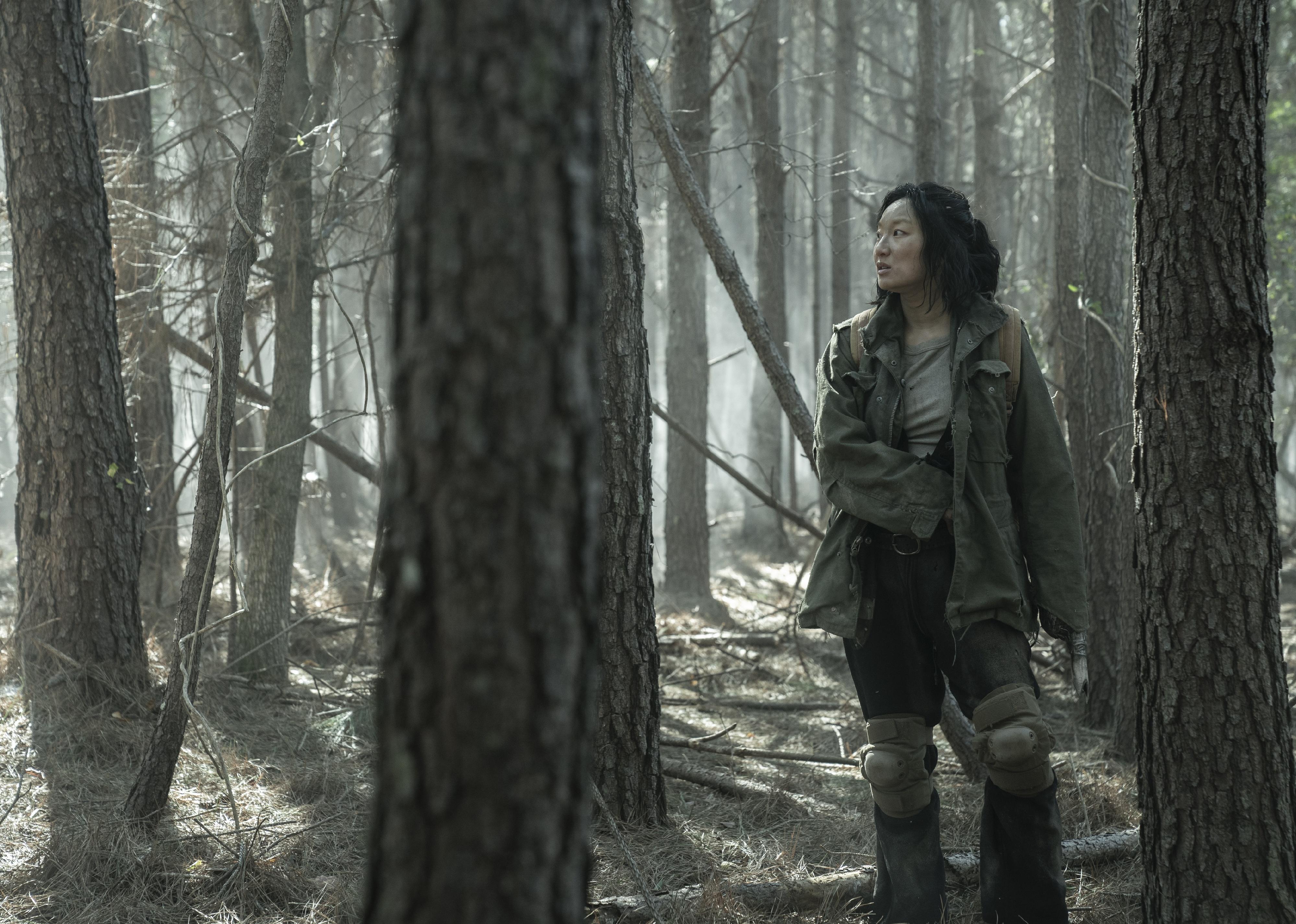 A woman in the woods wearing knee pads and dark tattered clothing.