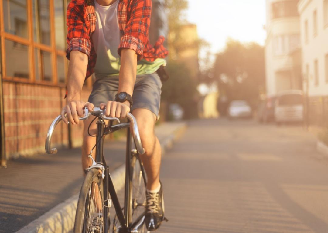 A man in a plaid shirt and shorts riding a bicycle.